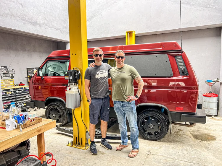 Two people beside a red Volkswagen Vanagon in the workshop