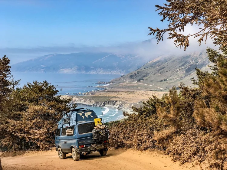 Blue Volkswagen camper overlooking a bay from a dirt road
