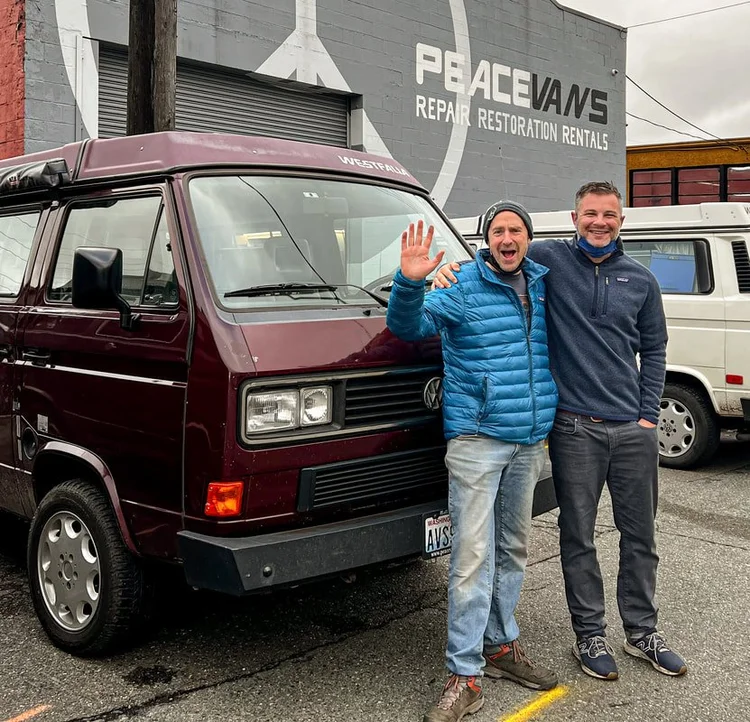 Two people beside a burgundy Volkswagen Vanagon