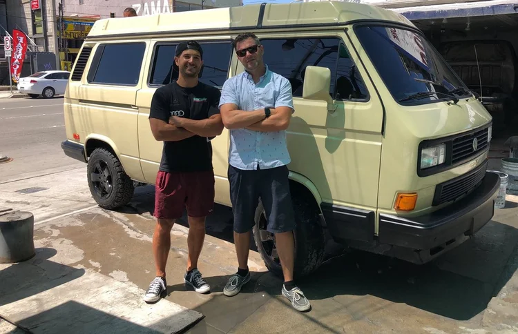 Two people beside a light green Volkswagen Vanagon