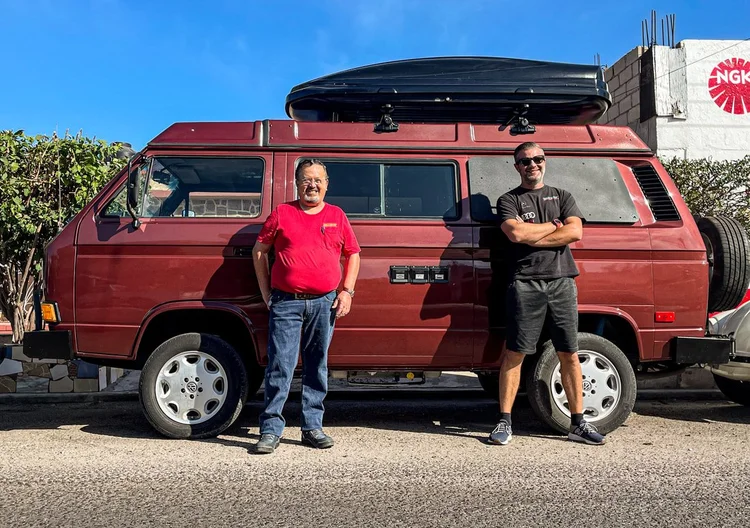 Two people beside a burgundy Volkswagen camper with roof cargo