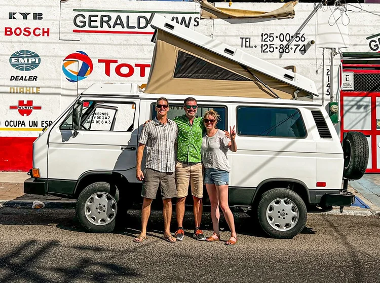 Three people beside a white Volkswagen Westfalia outside a workshop