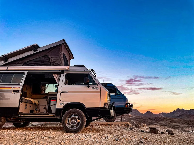 Volkswagen camper with open sliding door and raised pop-top at sunset