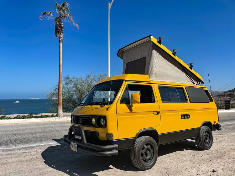 Yellow Volkswagen camper with raised pop-top by the waterfront