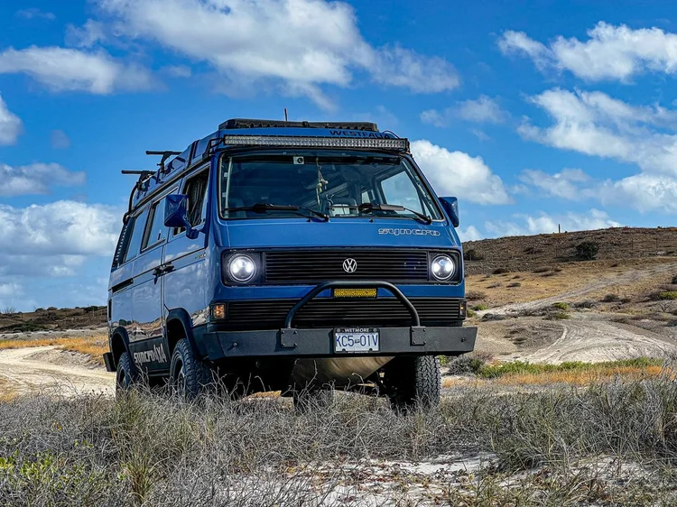 Blue Volkswagen camper parked in coastal scrub
