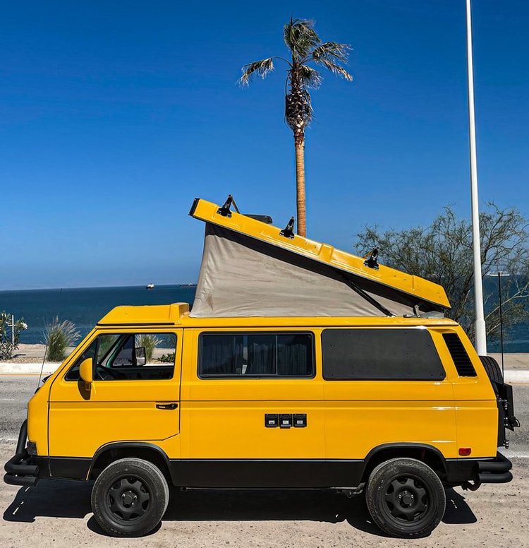 Side view of a yellow Volkswagen camper with raised pop-top