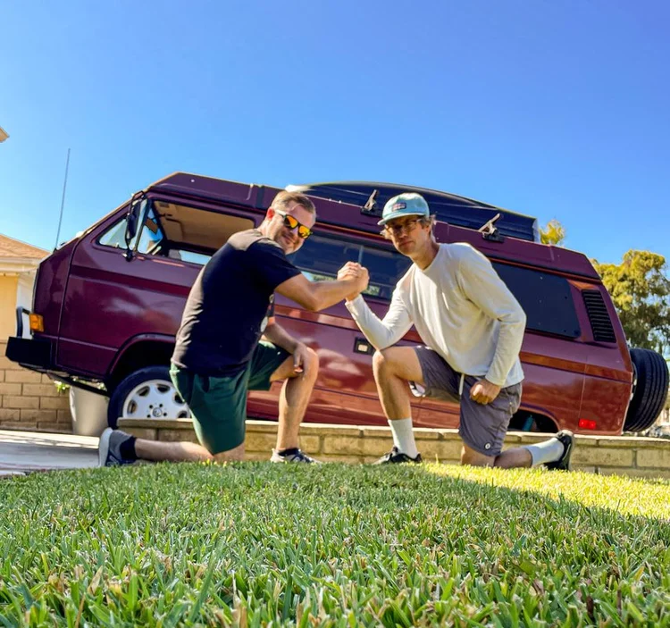 Three people beside a burgundy Volkswagen camper