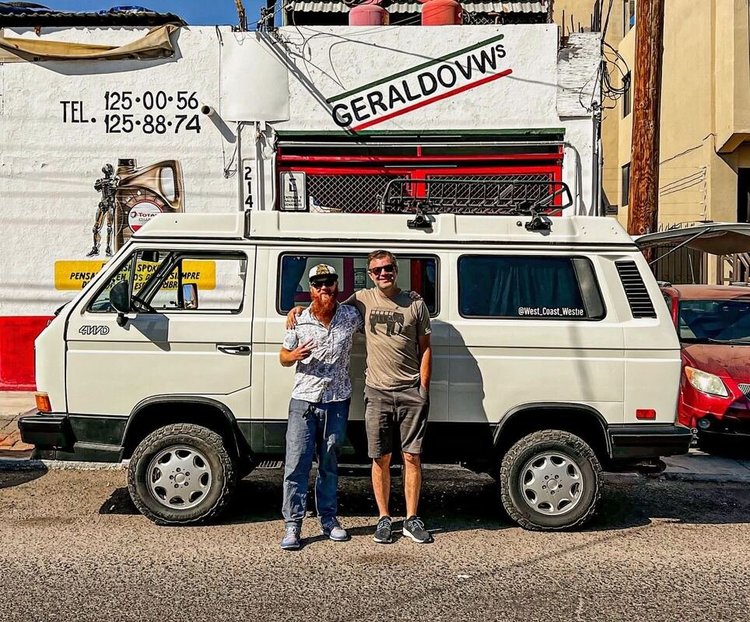 Two people beside a white Volkswagen camper outside a workshop