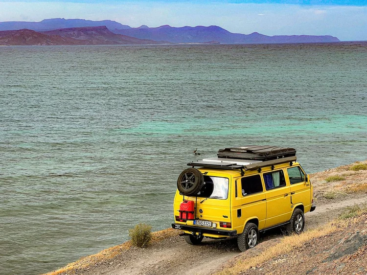 Yellow Volkswagen camper parked beside turquoise water