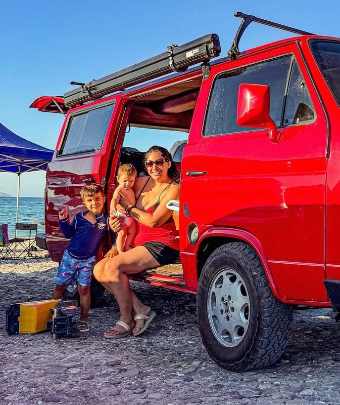 Two people sitting in the open sliding doorway of a red Volkswagen van