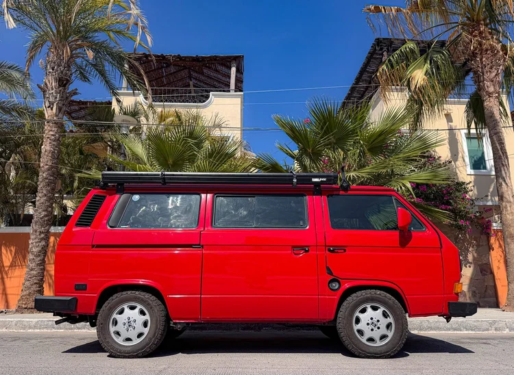 Side view of a red Volkswagen Vanagon beside a house