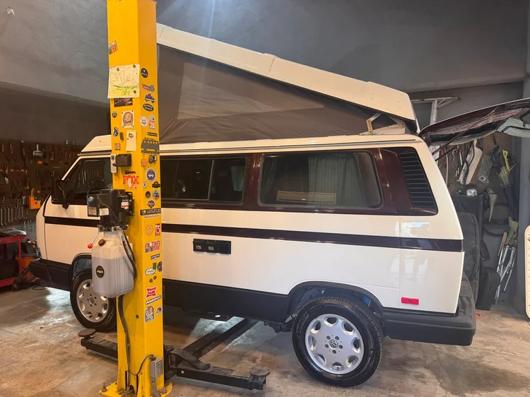 White Volkswagen camper with raised pop-top inside the workshop