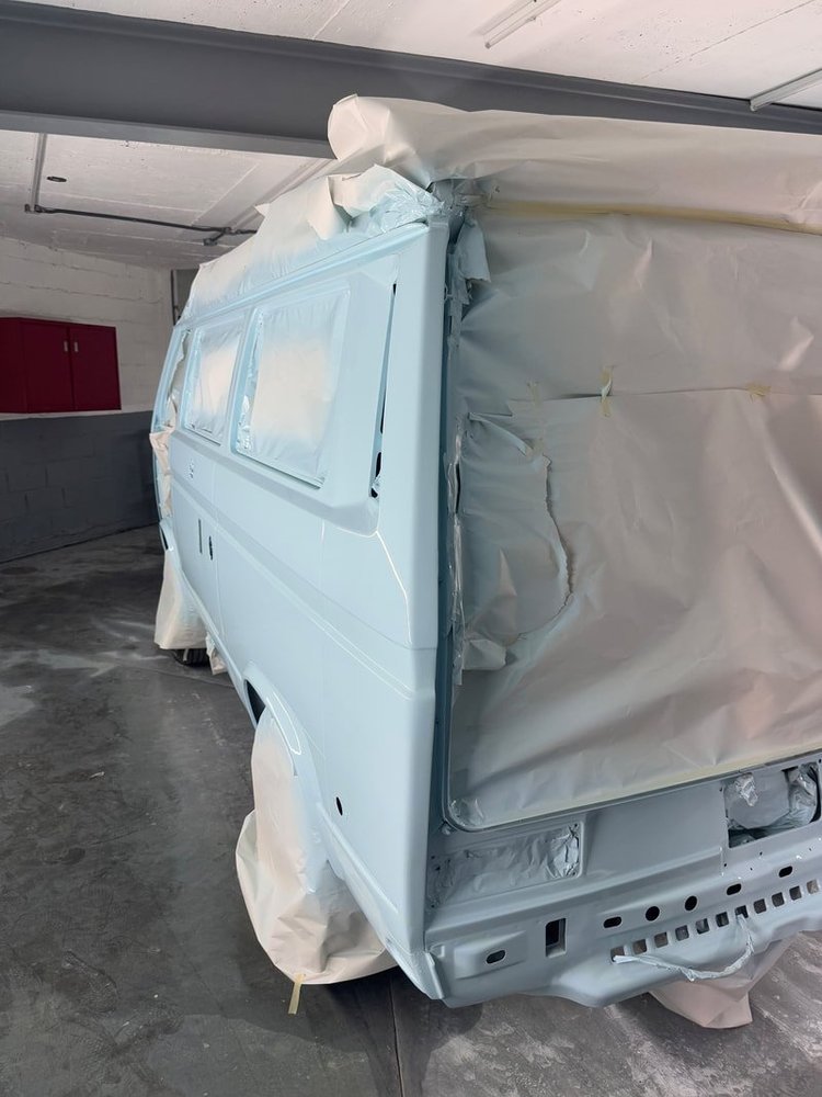 Rear corner of a light blue Volkswagen van in the spray booth