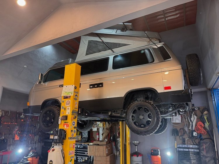 Cream Volkswagen camper with raised pop-top on a lift