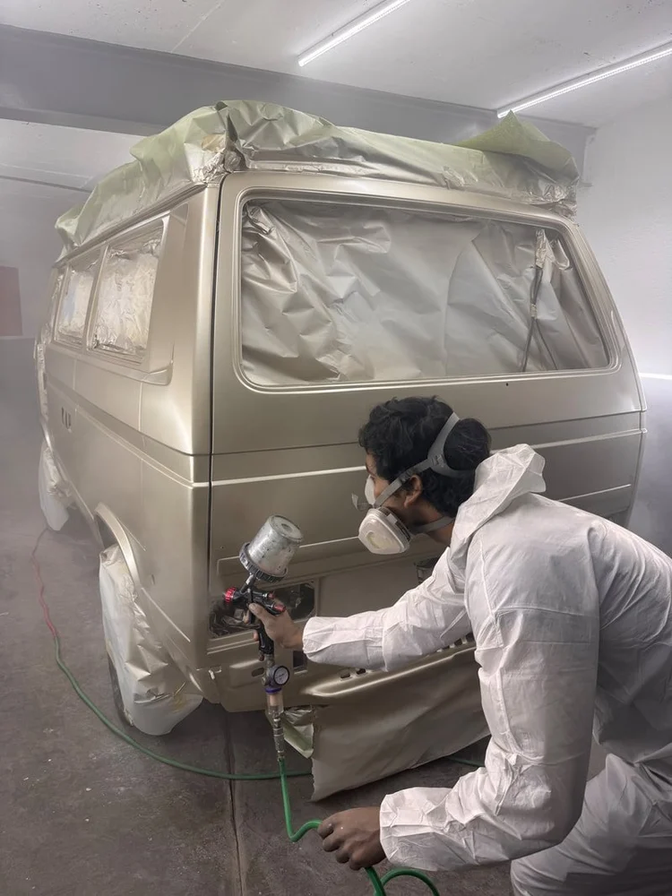 Painter spraying a masked Volkswagen van in the paint booth