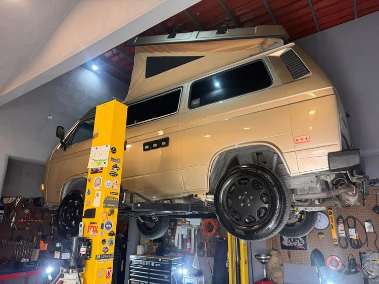 Rear three-quarter view of a cream Volkswagen camper on a lift