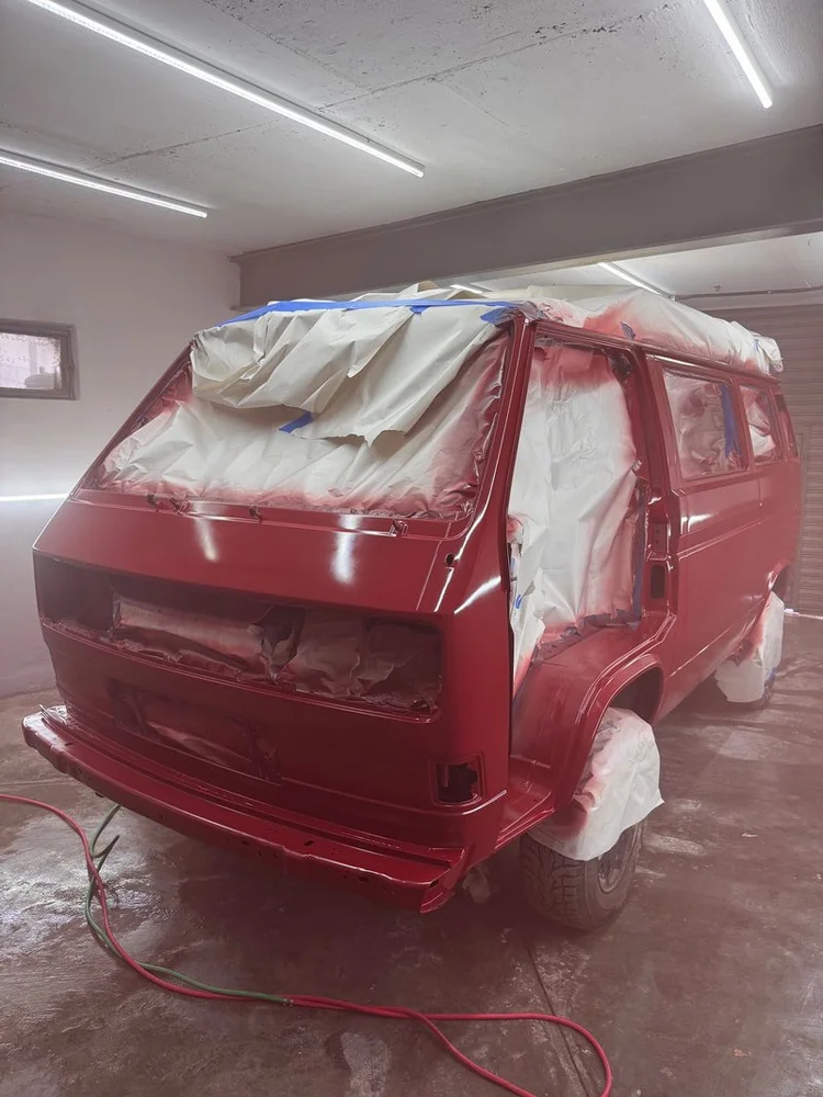 Front of a red Volkswagen van with windows masked for painting