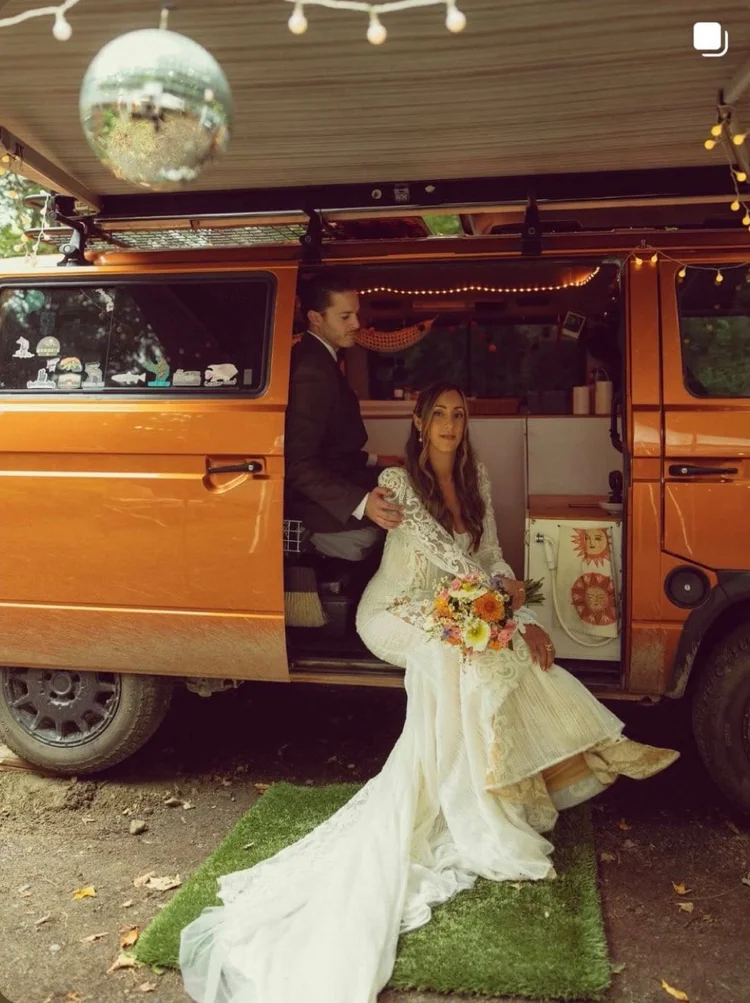 Bride beside an orange Volkswagen camper at a wedding