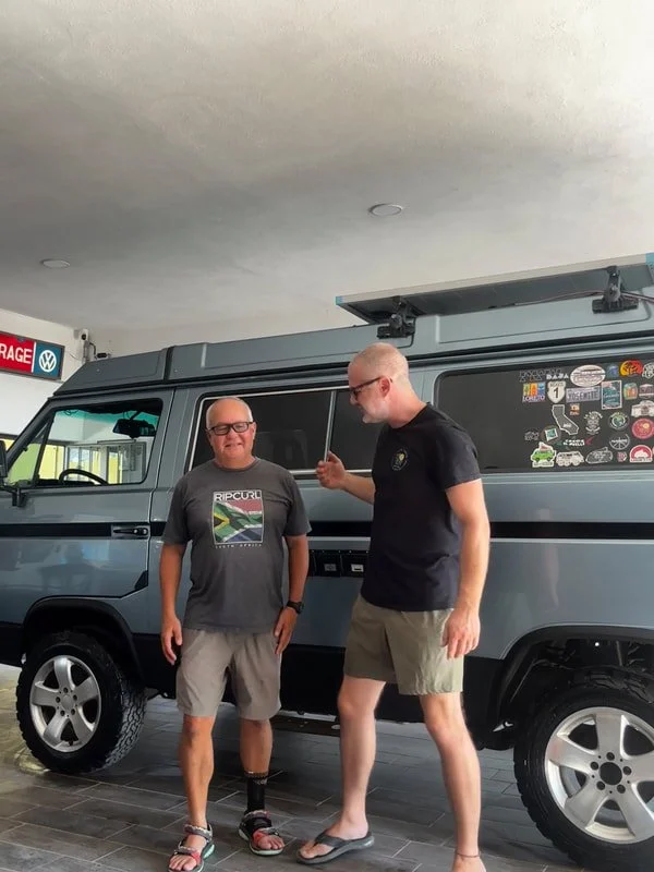 Two people beside a blue Volkswagen camper