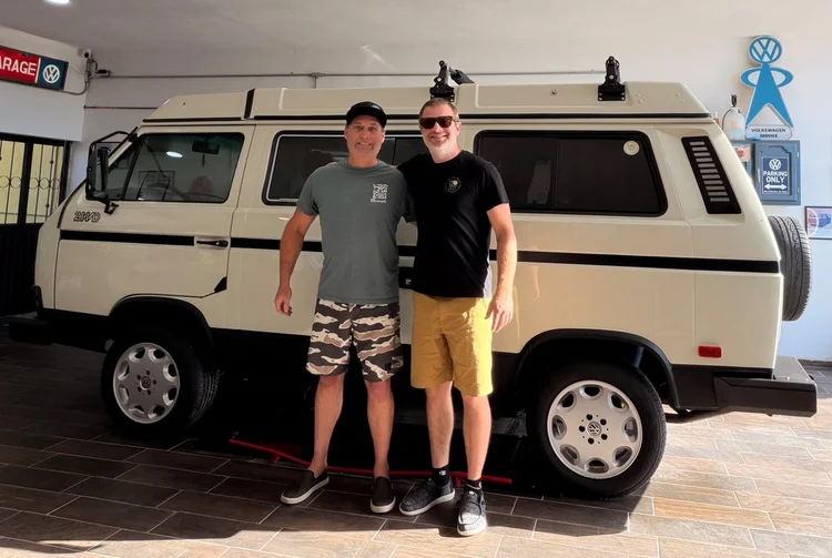 Two people beside a cream Volkswagen camper inside the workshop