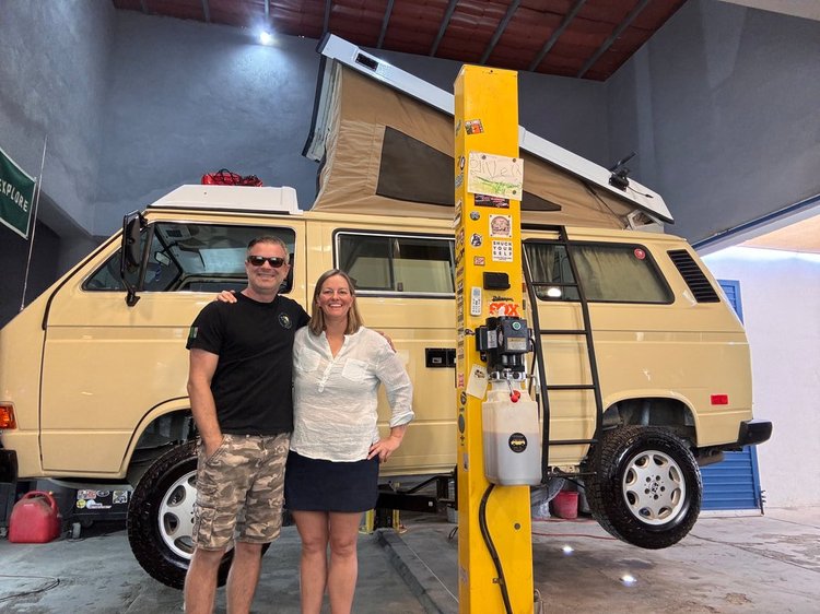 Two people beside a cream Volkswagen Westfalia in the workshop
