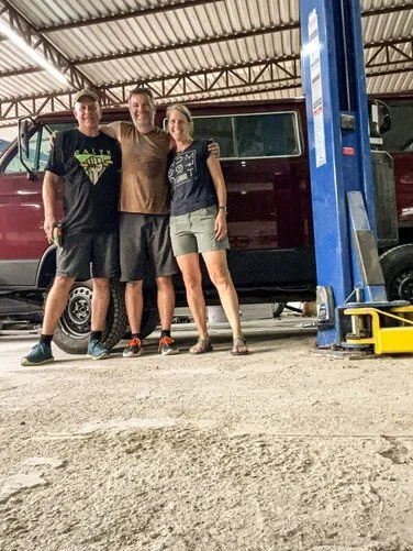 Three people in front of an open Volkswagen camper in the workshop