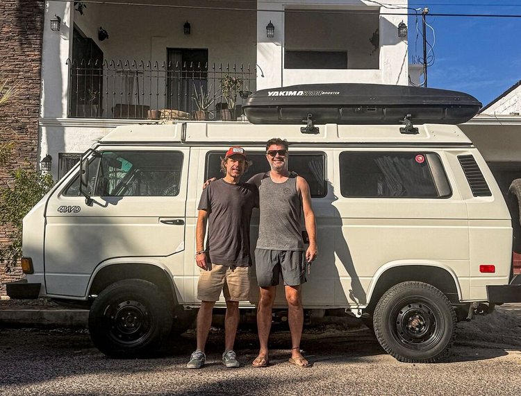 Two people beside a cream Volkswagen camper with roof cargo