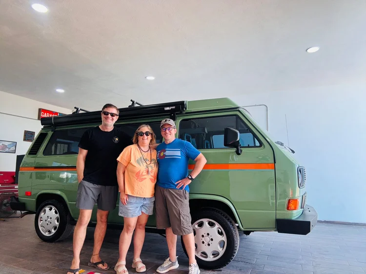 Three people beside a green Volkswagen Vanagon in the workshop