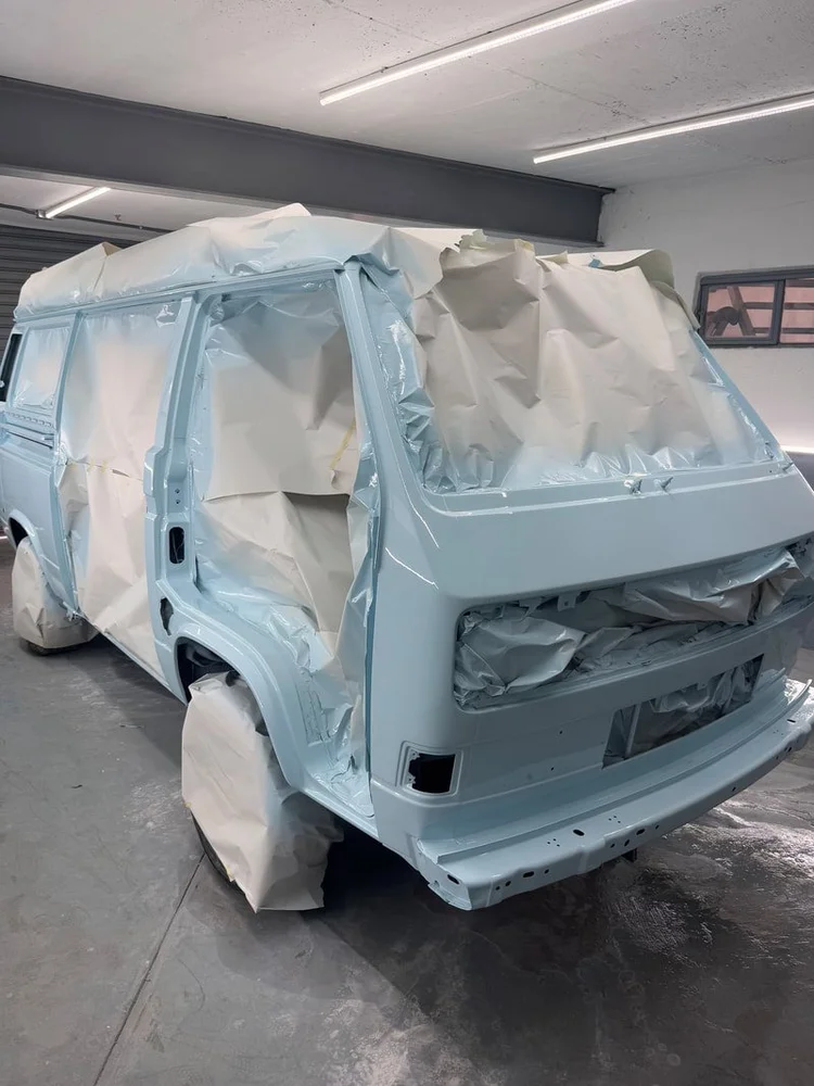 Light blue Volkswagen van masked for paint in the spray booth