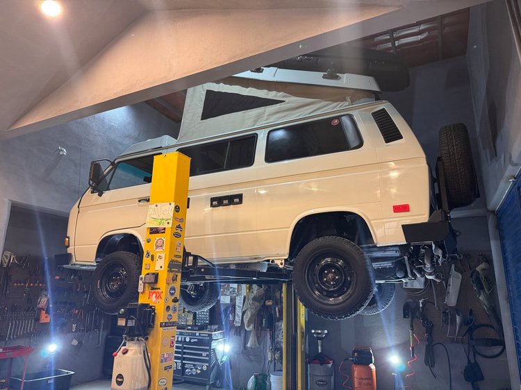 Cream Volkswagen Vanagon with black wheels on a workshop lift