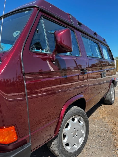 Burgundy Volkswagen camper showing the side door and front wheel