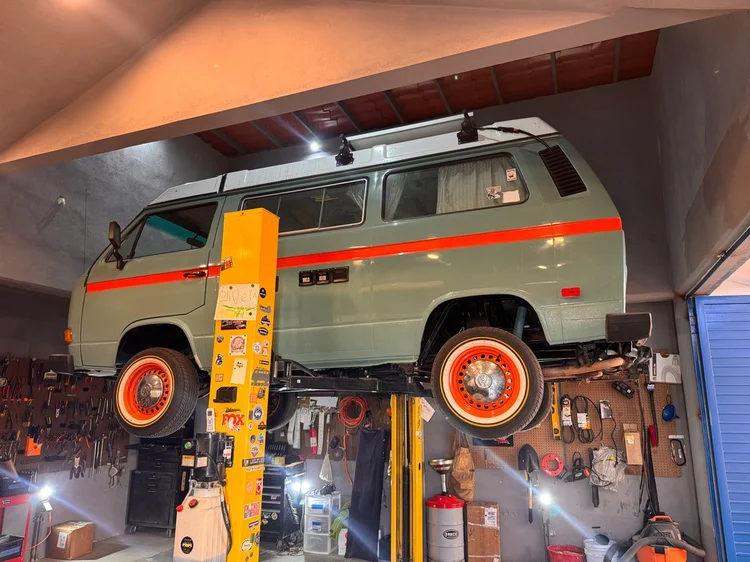 Gray Volkswagen camper with orange stripe and orange wheels on a lift