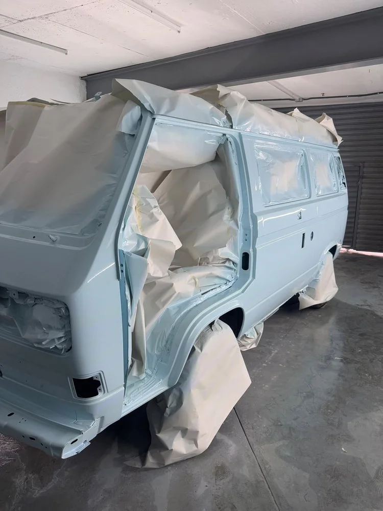 Side of a light blue Volkswagen van with windows masked for painting