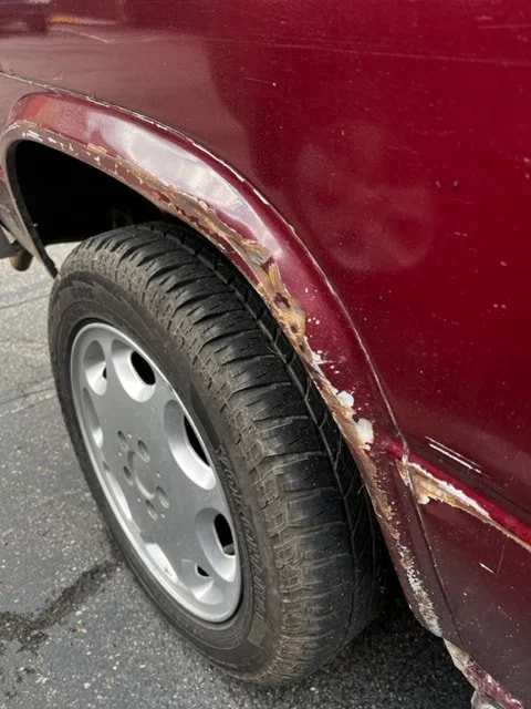 Close-up of worn paint around a burgundy Volkswagen wheel arch