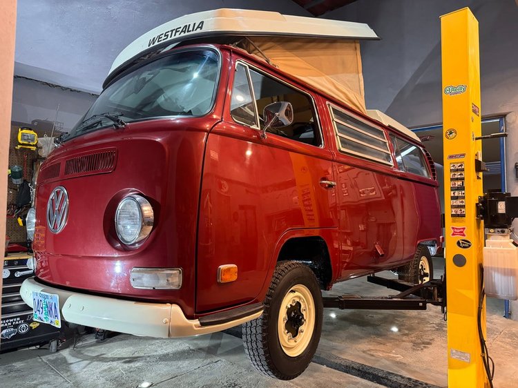 Front three-quarter view of a red Volkswagen Bus on a workshop lift