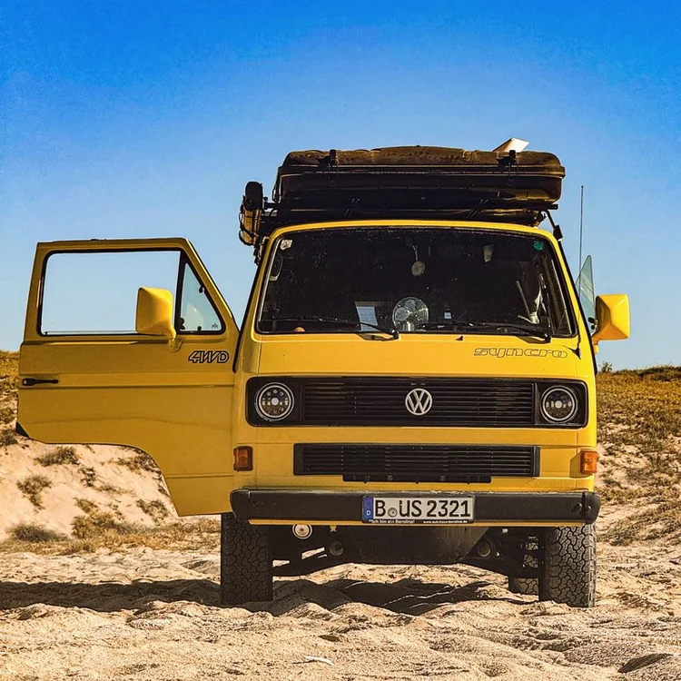 Yellow Volkswagen Vanagon on sand with the driver's door open
