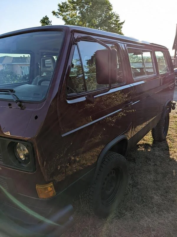 Front quarter of a burgundy Volkswagen van parked beside a house