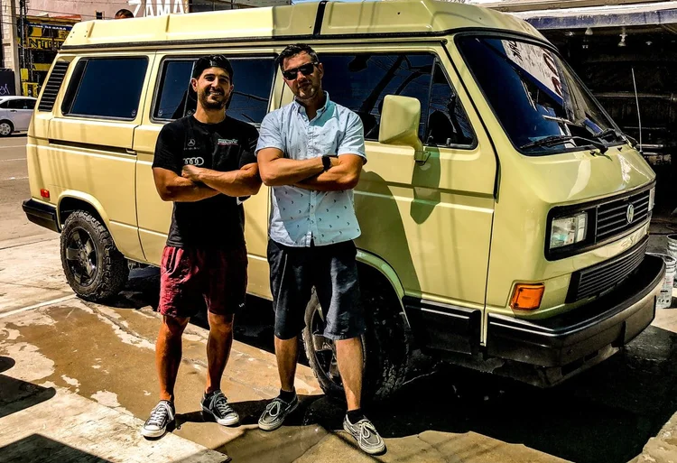 Two people beside a light green Volkswagen Vanagon