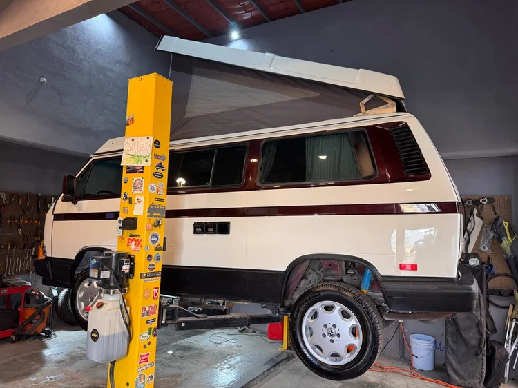 White Volkswagen camper with brown stripe and raised pop-top on a lift