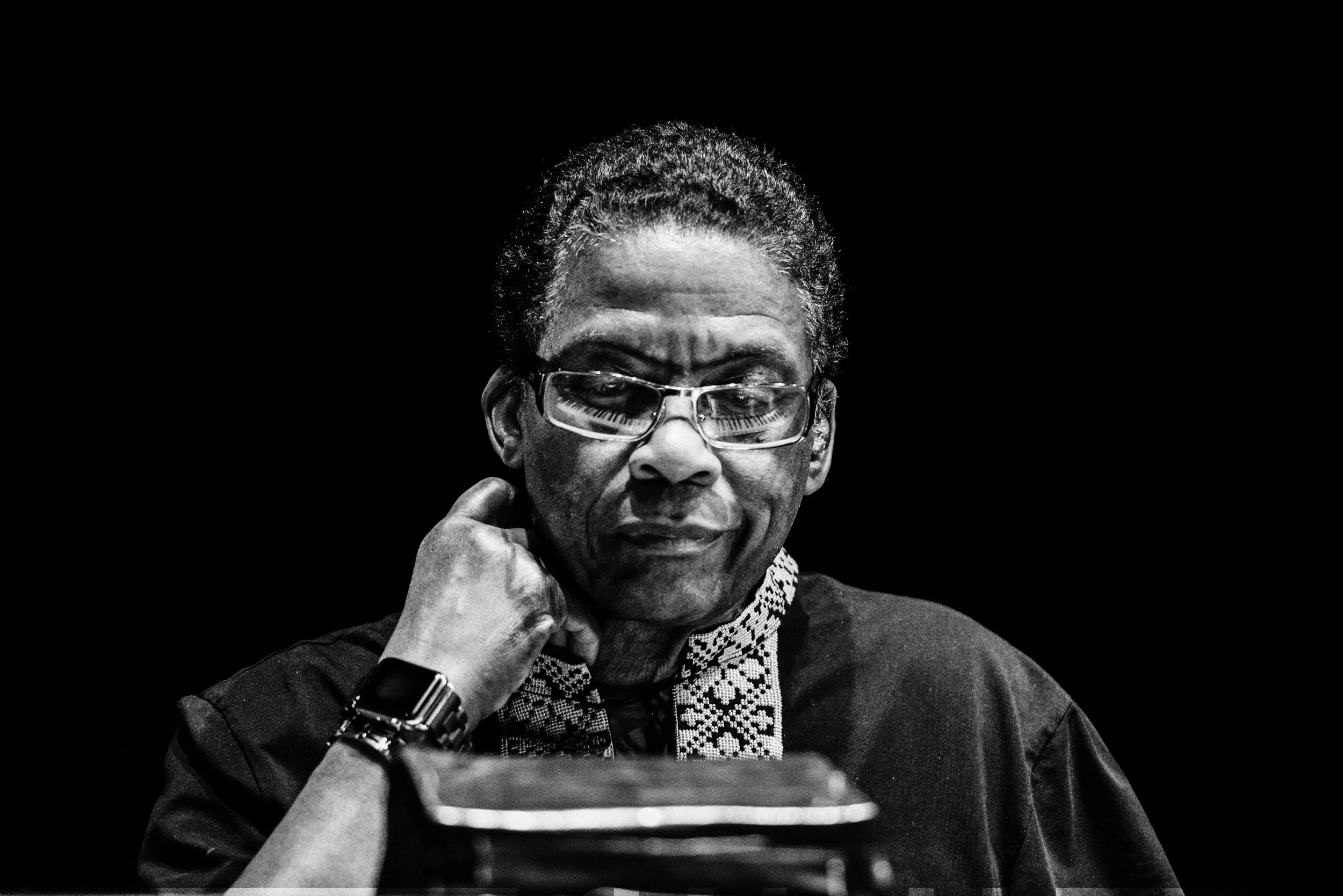Black-and-white portrait of a man wearing glasses, resting his chin on his hand.
