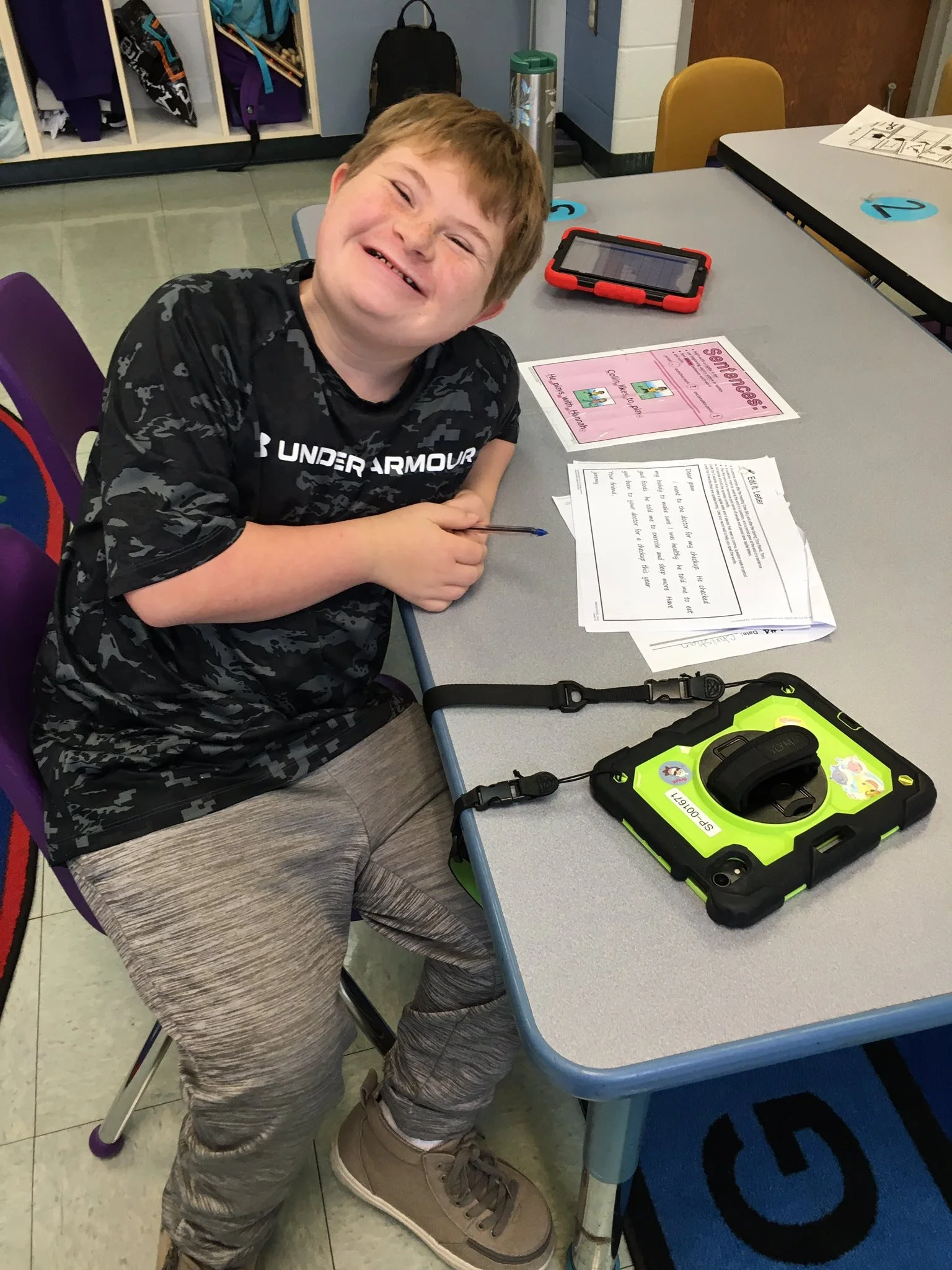 A Dale-Roy School student smiling at his classroom desk, with a tablet and worksheet in front of him — ready to learn.