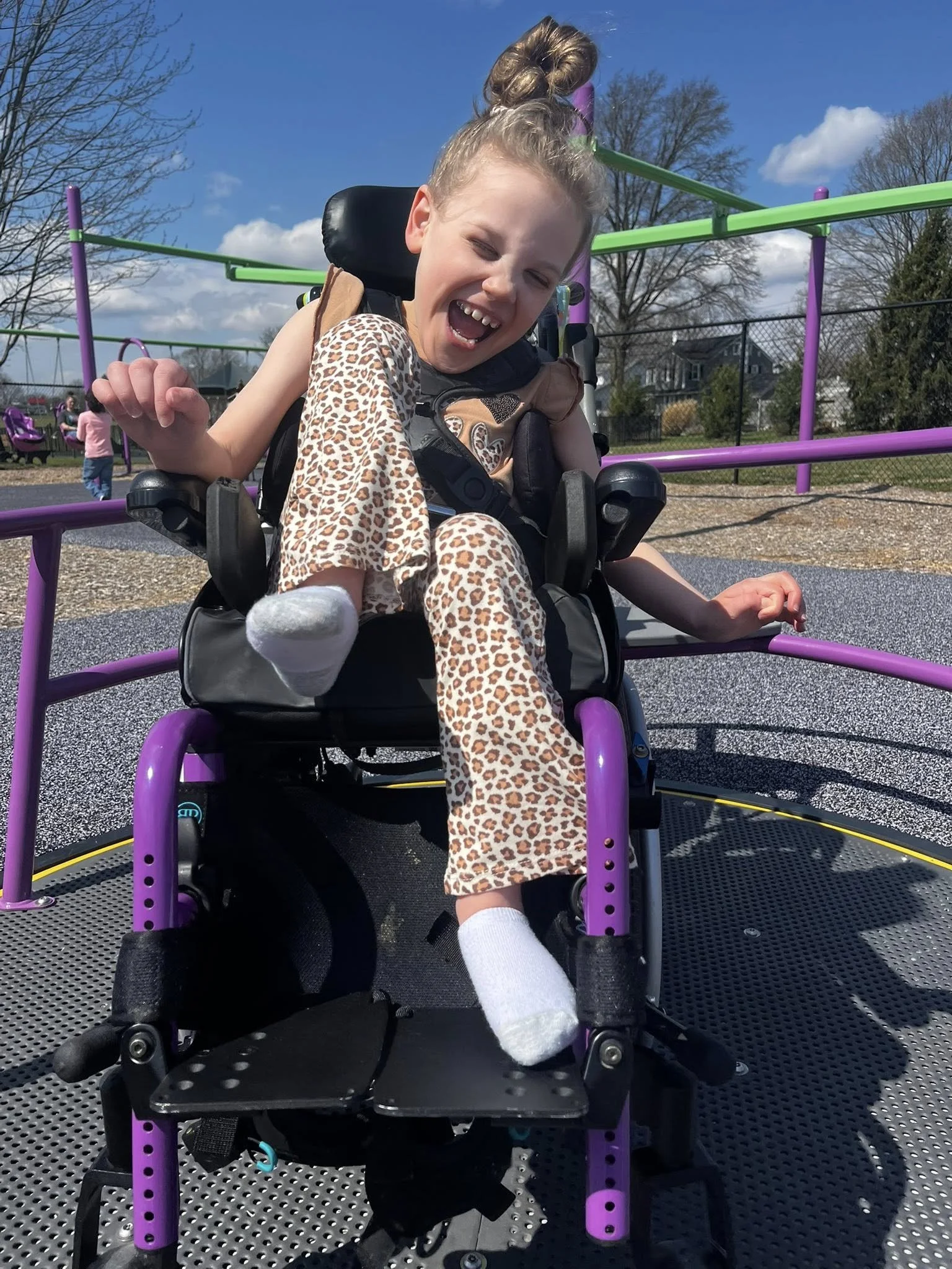A Dale-Roy School student laughing with joy on accessible playground equipment on a sunny day.