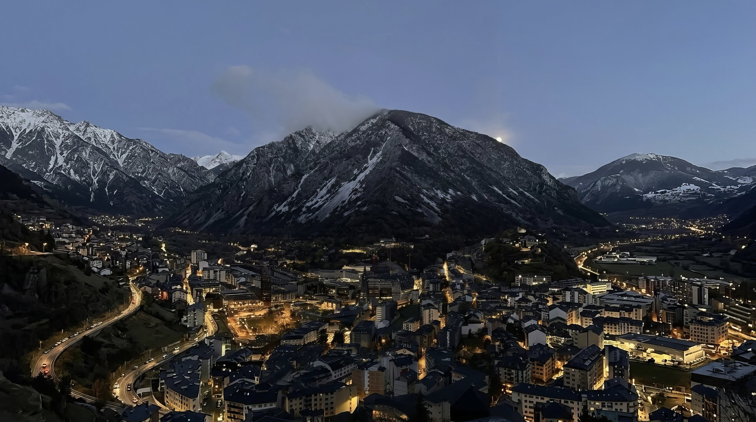 Andorra la Vella at dusk — alpine valley framed by snow-capped peaks, town lights below