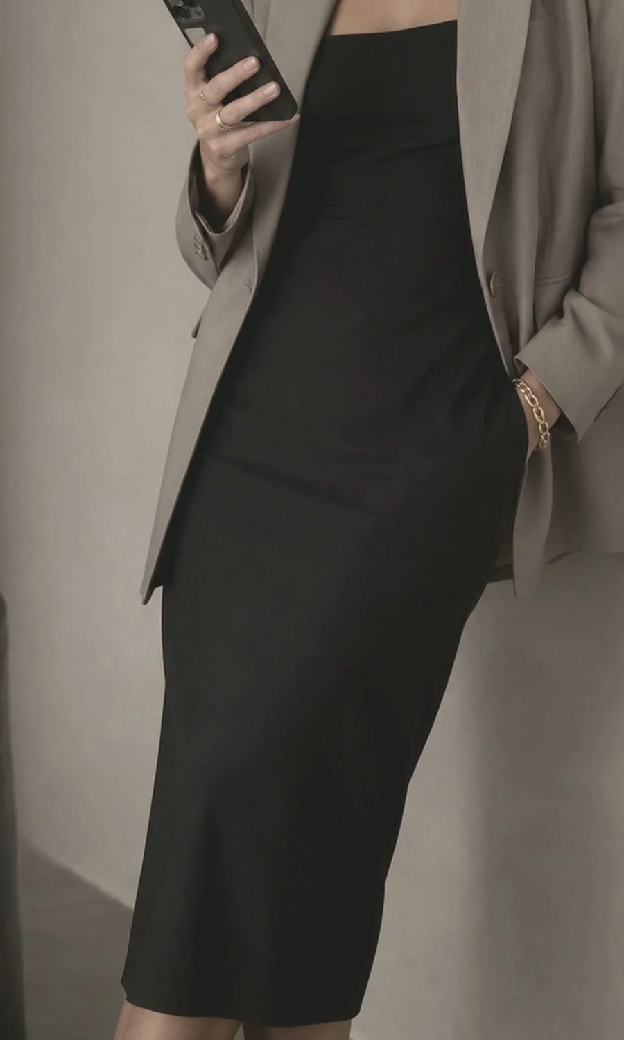 A woman standing against a plaster wall, phone in hand