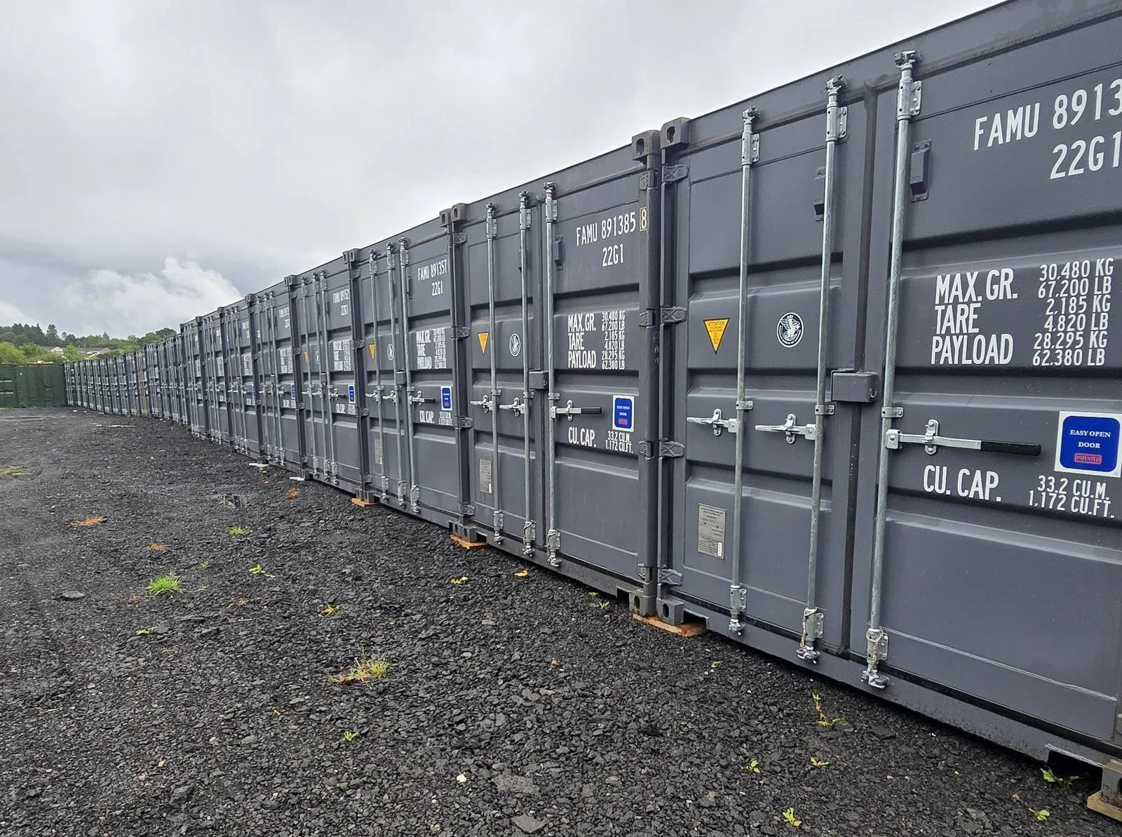 A long row of dark grey storage containers on the hard standing at JT Self Storage