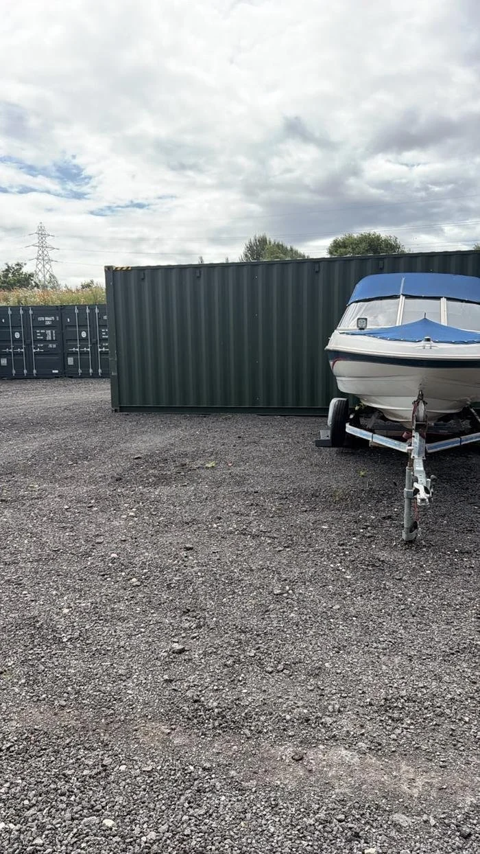 A boat on a trailer stored beside a green container