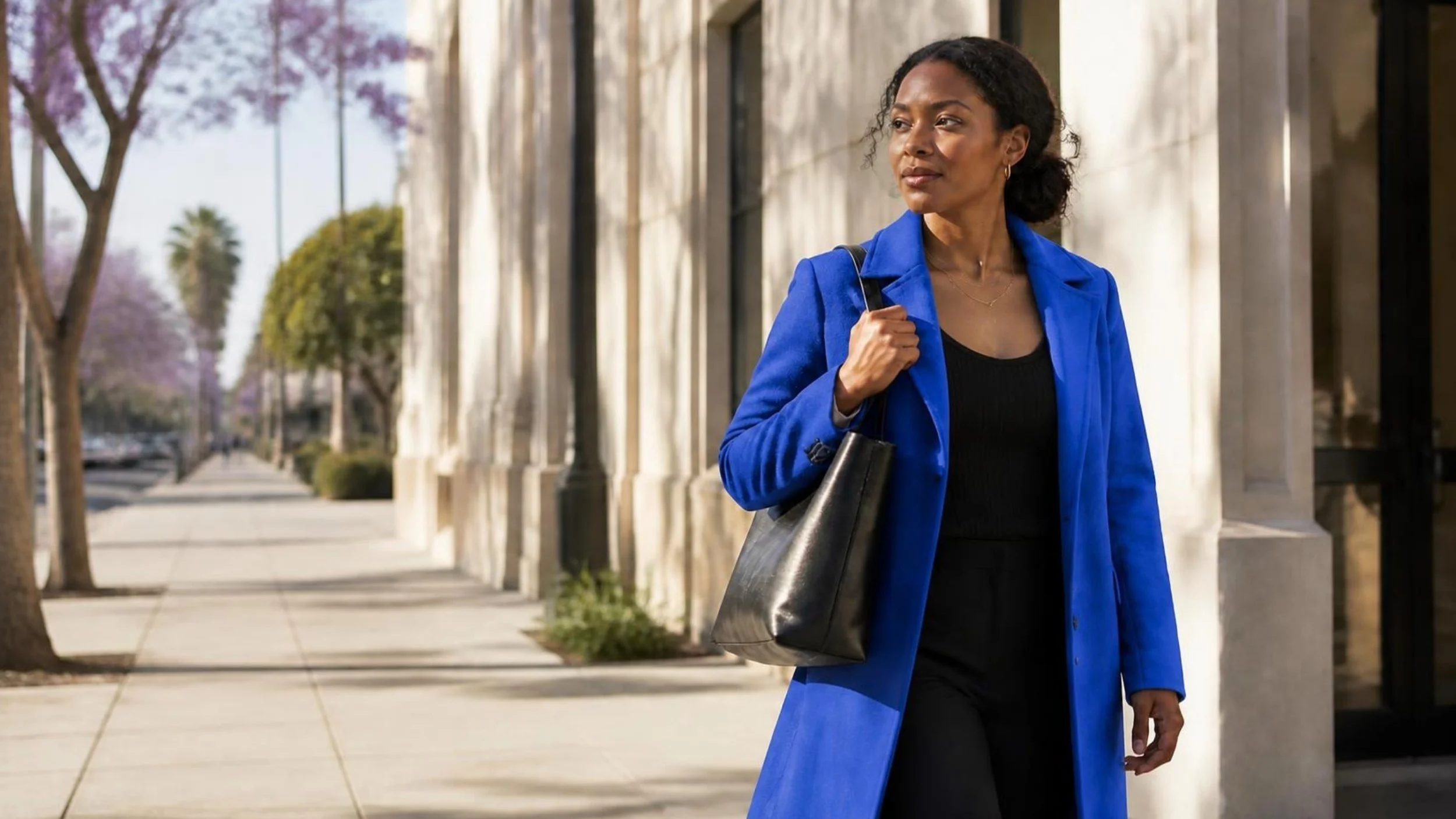 A woman in a cobalt coat walking to work on a sunny morning street