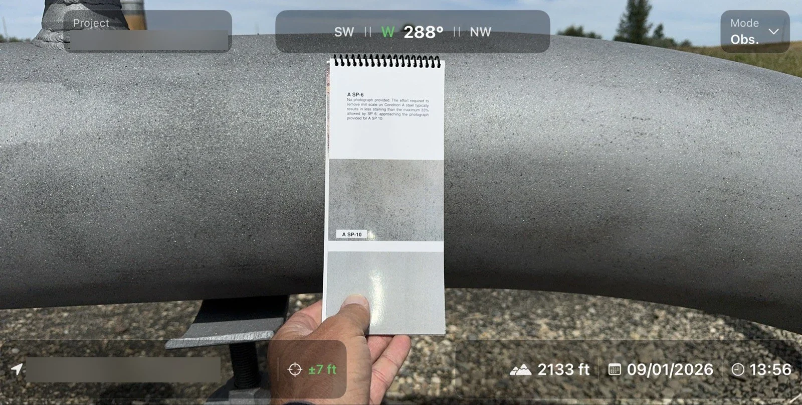 Hand holding a surface comparator card against a coated pipe