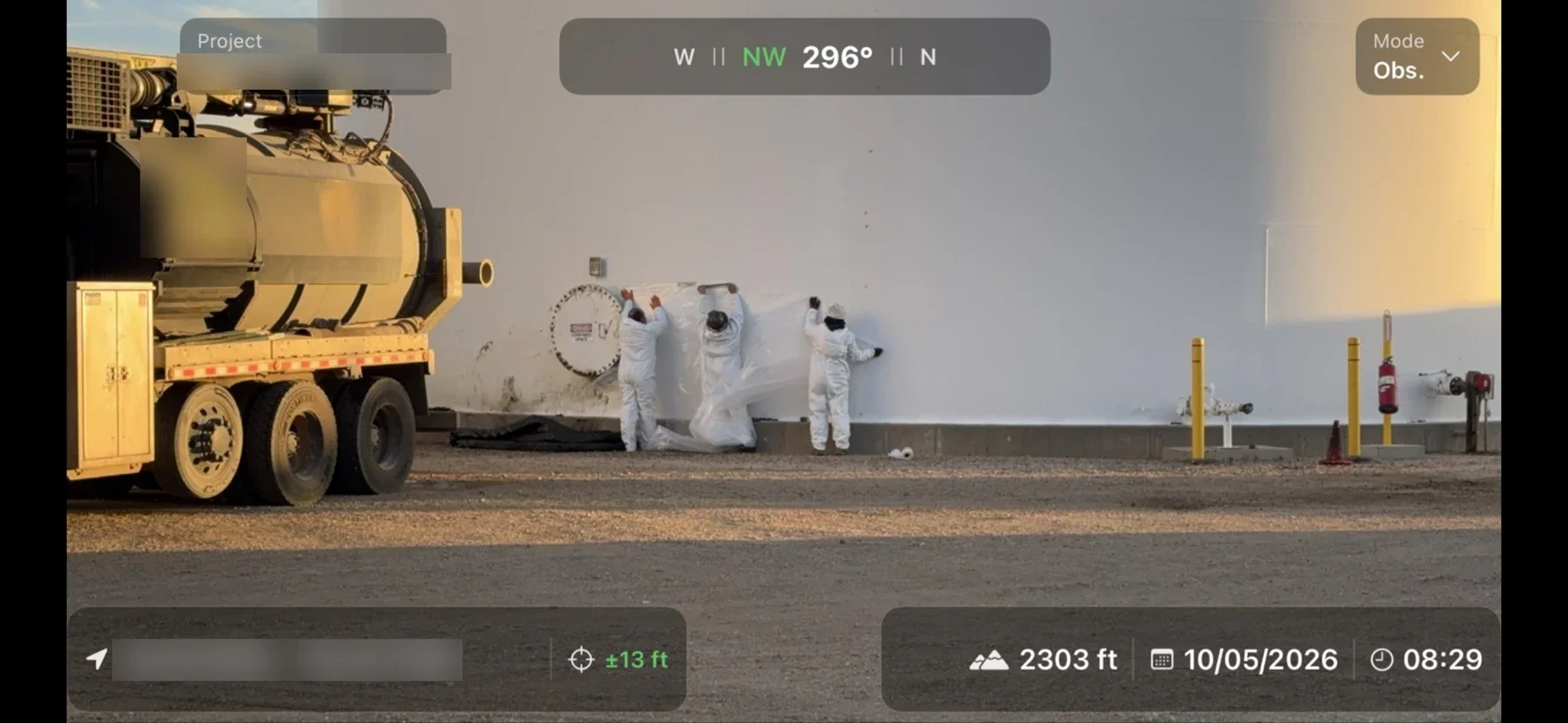 Crew in protective suits working at the base of a large storage tank beside a vacuum truck