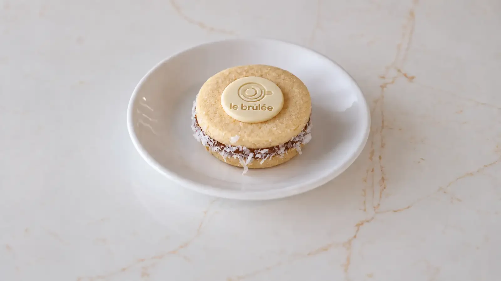 Le Brulée Café classic alfajor with coconut edges and a branded chocolate medallion